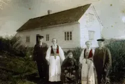 Tre kvinner og to menn framfor ei vestlandstove. Mor med dotter og son på si venstre side.