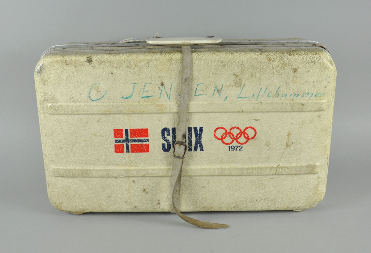 Slitt hvit koffert med OL-ringer og norsk flagg. Kofferten inneholder skismøring fra 1970-tallet.