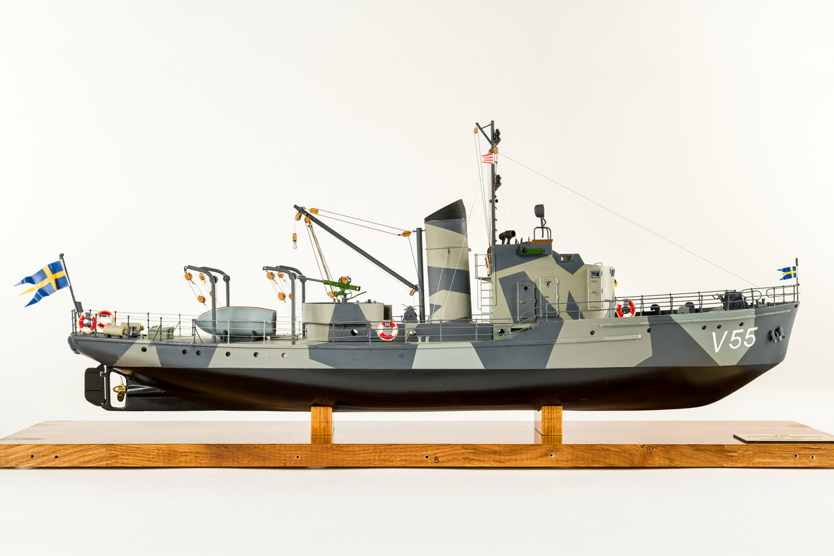 Fartygmodell av vedettbåten V 55 av plywood, plast och metall. Kamoflagemålad i grått. Notera särskilt sjökortet över Göteborgs skärgård, det var där fartyget hade sin hemvist. Däck tillverkat av 2 mm plywood. Däckshus, ankarspel, ankare, skeppsbåt, sjunkbomber och livbojar är av plast och utskrivna med 3D-skrivare. Målad med acrylfärg som antingen sprutmålats eller penselmålats.

Modellen står i plexiglasmonter på fernissad träplatta med informationsskylt.