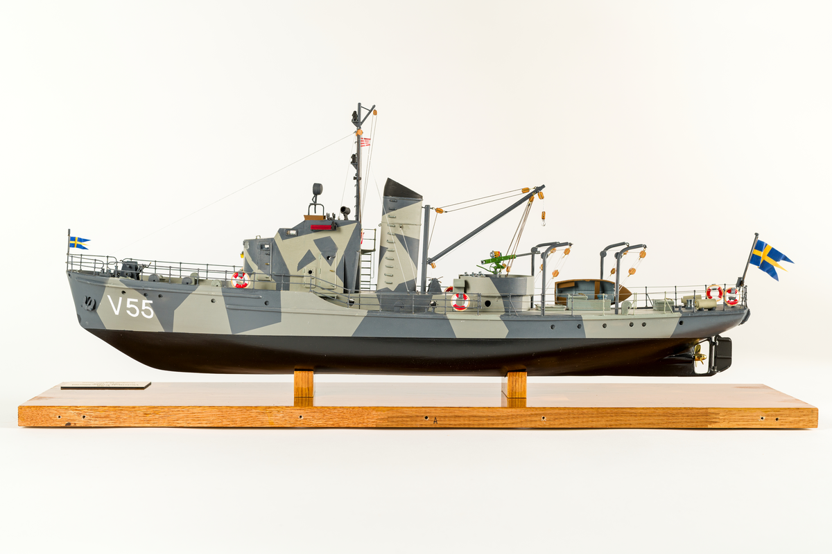 Fartygmodell av vedettbåten V 55 av plywood, plast och metall. Kamoflagemålad i grått. Notera särskilt sjökortet över Göteborgs skärgård, det var där fartyget hade sin hemvist. Däck tillverkat av 2 mm plywood. Däckshus, ankarspel, ankare, skeppsbåt, sjunkbomber och livbojar är av plast och utskrivna med 3D-skrivare. Målad med acrylfärg som antingen sprutmålats eller penselmålats.

Modellen står i plexiglasmonter på fernissad träplatta med informationsskylt.