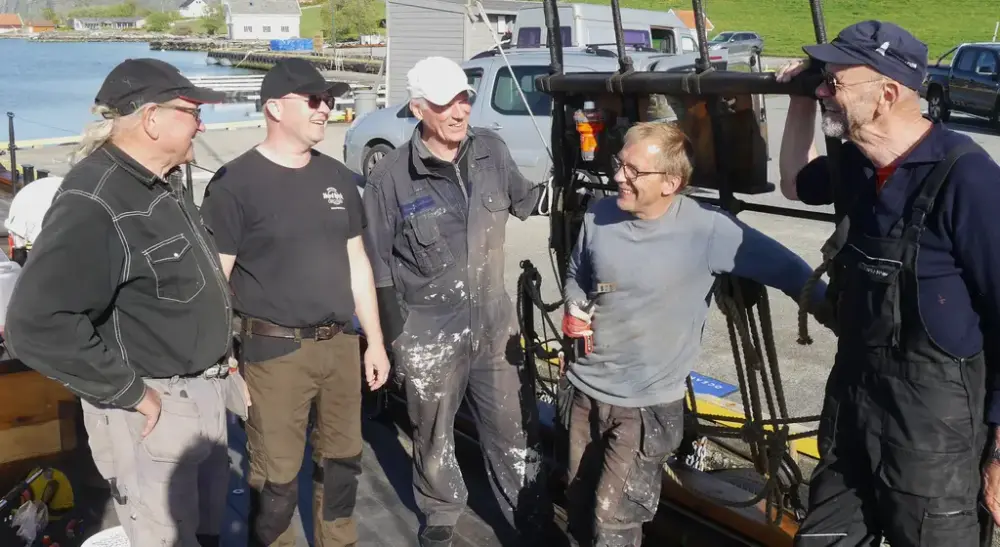 Fem menn i arbeidstøy snakker snammen på kai. Biler i bakgrunn.