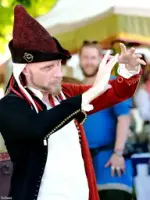 Mann i rød spiss middelalderhatt, rød og svart middelalderdoublet og hvit linskjorte som får en ring til å sveve i løse luften