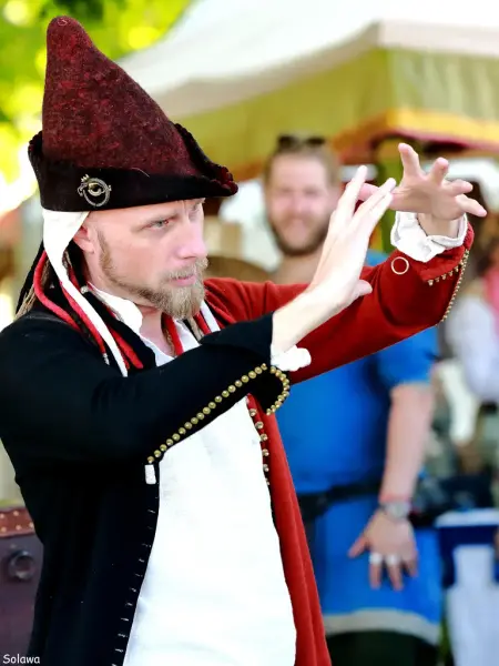 Mann i rød spiss middelalderhatt, rød og svart middelalderdoublet og hvit linskjorte som får en ring til å sveve i løse luften