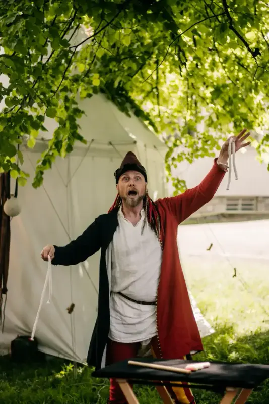 middelaldermagiker i rød, svar og hvit cotehardi som gjør magitriks