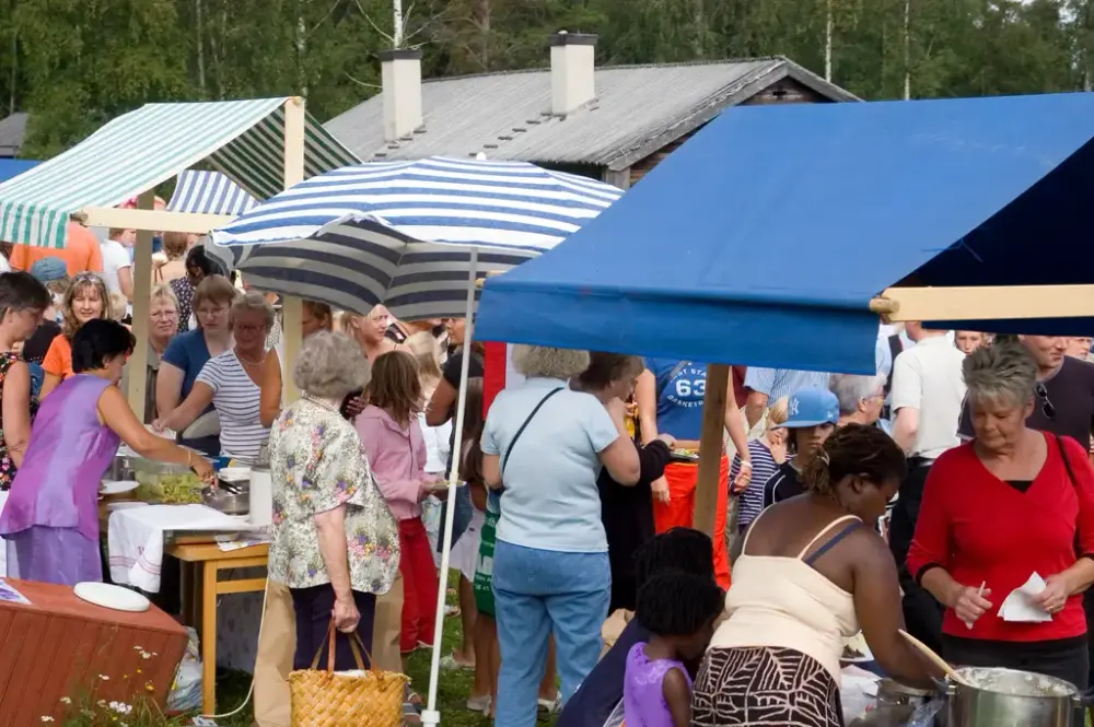 Matstånd med stor folksamling runt omkring. Hus med skorstenar i bakgrunden.