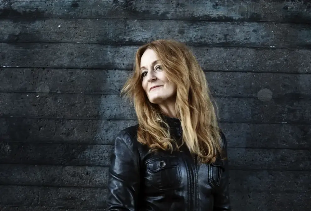 En kvinna i svart jacka står framför en mörk bakgrund.