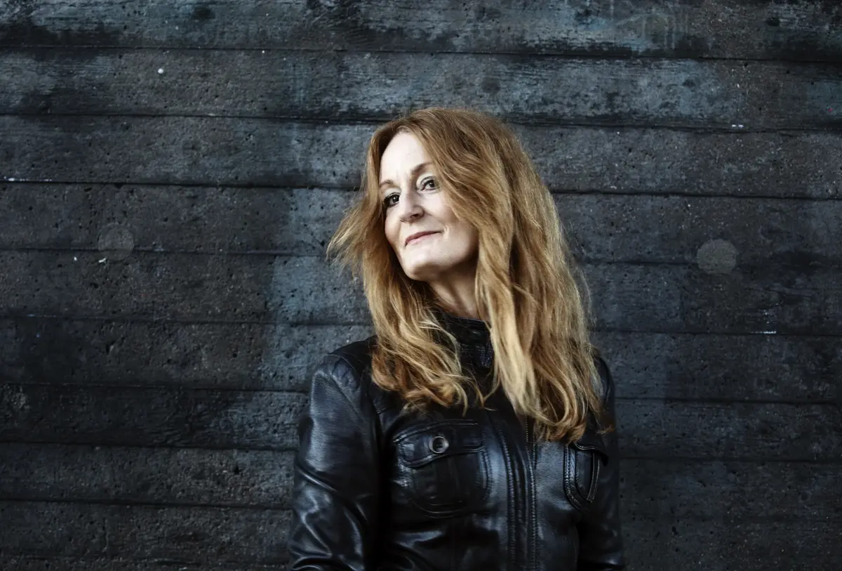 En kvinna i svart jacka står framför en mörk bakgrund.