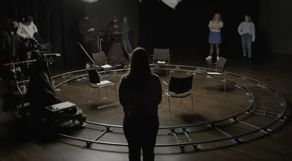 Kunstverk. Mennesker i et mørkt rom med stoler i sirkel