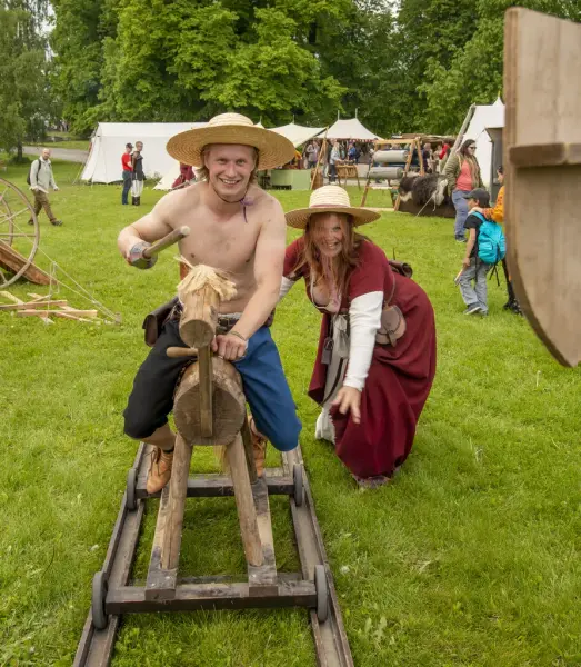 Ung mann på trehest med lanse. Dyttet av kvinne i rød middelalderkjole