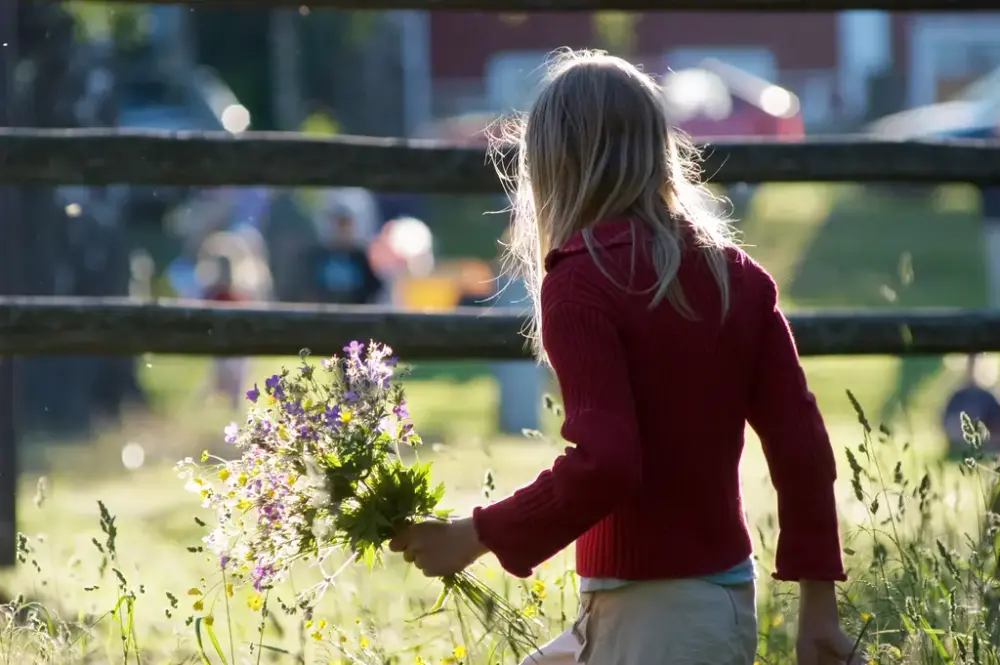 Flicka med blombukett går i en blommande äng.