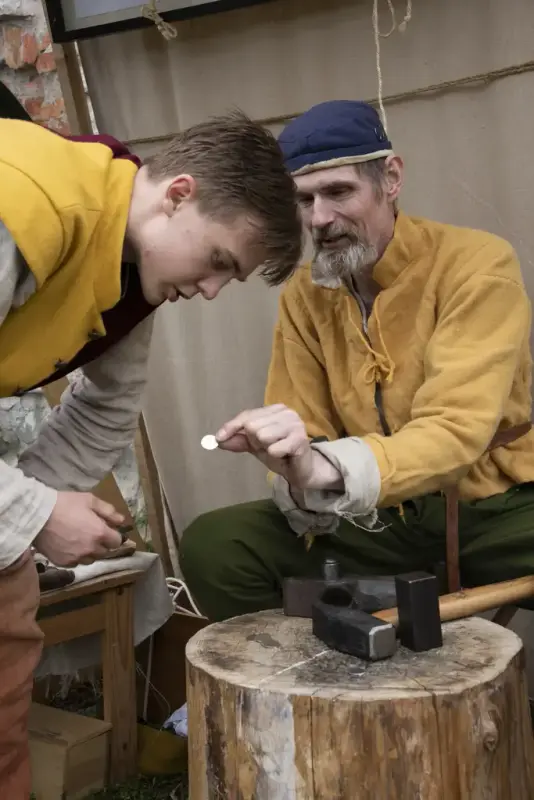 Mann i middelalderklær som har slått mynt og viser fram til en ung gutt i middelalderklær