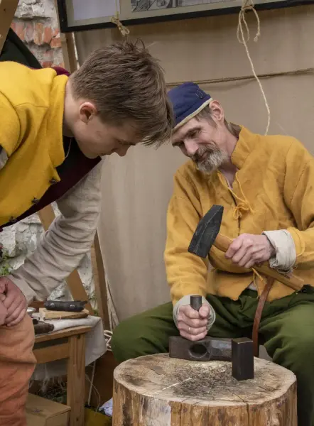 Mann i middelalderklær demonstrerer myntslaging for ung mann i middelalderklær