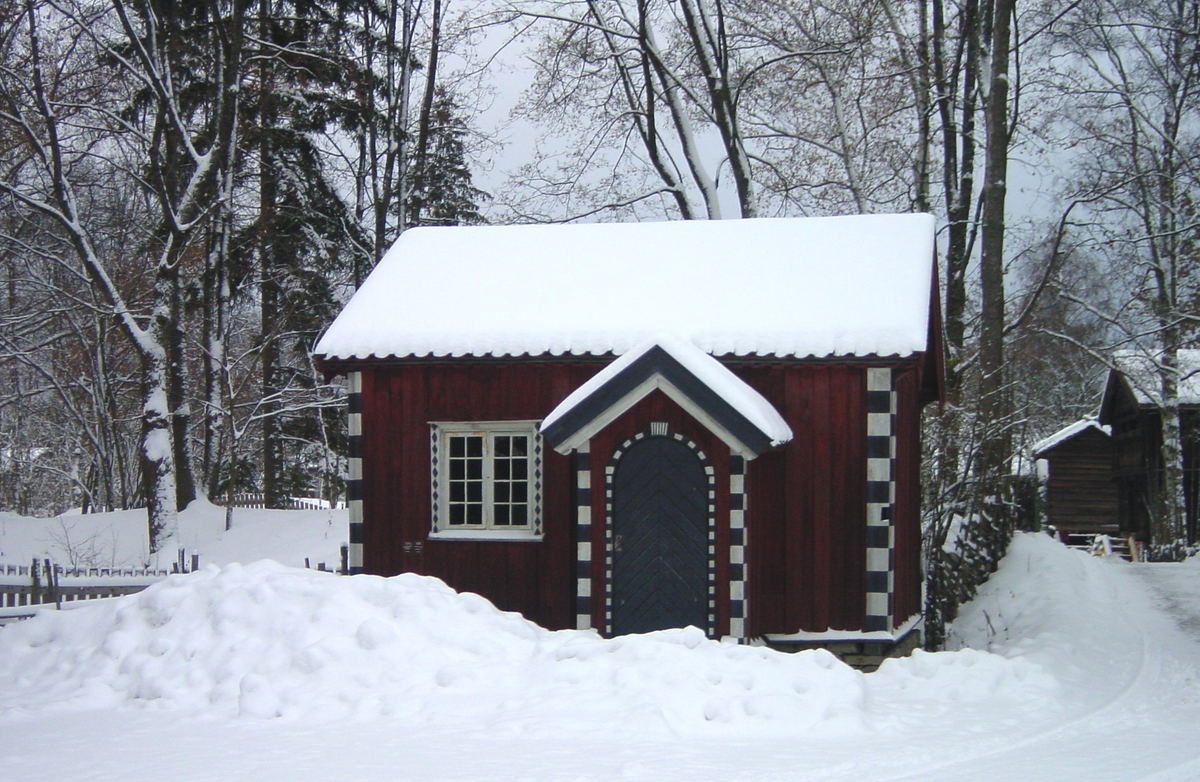 STUE FRA AKKERHAUGEN I SAUHERAD, CA. 1800 
Overført til museet 1909, gjenoppført 1910 

Stua, på folkemunne kalt «Cappelenstugu», er bordkledd og rødmalt, og hjørnene er malt med svarte og hvite kvadrater. Fargene skulle illudere teglmur med detaljer i stein. Skikken er lånt fra byhus i Porsgrunn og Skien, som igjen er malt etter forbilder fra utenlandske byer. 

Stua, som er rikt dekorert, består av ett rom med et lukket bislag foran inngangsdøra. Sengene og skapene hører med til det originale interiøret. I et hjørne har det vært peis. Møblene er smykket med flatskurd. Interiøret ble malt av den kjente rosemaleren Olav Hansson fra Hovin, som var mester for en rekke dekorerte stuer. Hver vegg har sitt motiv, omrammet av «roser»: dyret i lenker fra Johannes’ Åpenbaring, syndefallet, Samson og løven – og til sist hverdagsmotivet med bonden og tømmermerkeren. Initialene på framskapet – HOS LID – står for Halvor Olsen og Liv Johannesdatter. 

(Tekst hentet fra By og bygd 43, 2010)
