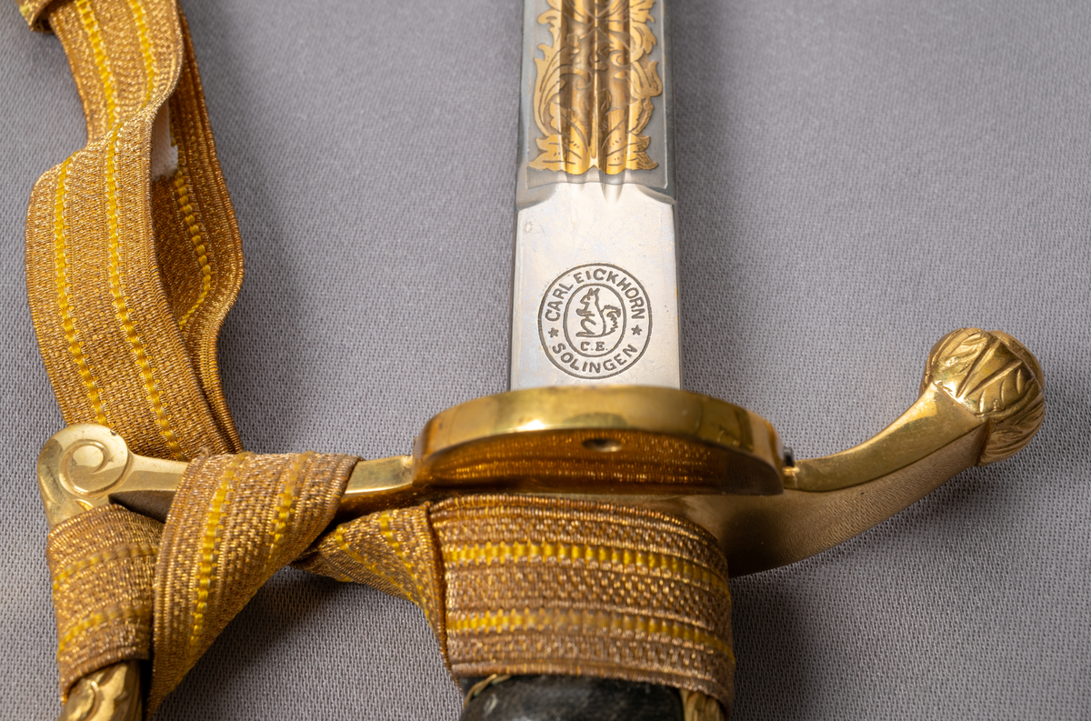 Sabel med portepé och balja, för kommisarie eller högre befattning. Rak dubbeleggad klinga med dubbla blodrännor. Ornament i i guld med text "Konungen" och "Fäderneslandet" samt lilla riksvapnet och nordstjärnan på klingans vardera sida. Mörkbrunt fäste med tvinnad metalltråd i guldfärg, hel fästkappa som övergår i ett lejonhuvud. Parerplåten prydd med lilla riksvapnet. Baljan är av läder med ornamenterat munbleck och beslag med släpsko i förgylld metall. Portepé i gulddrageri.