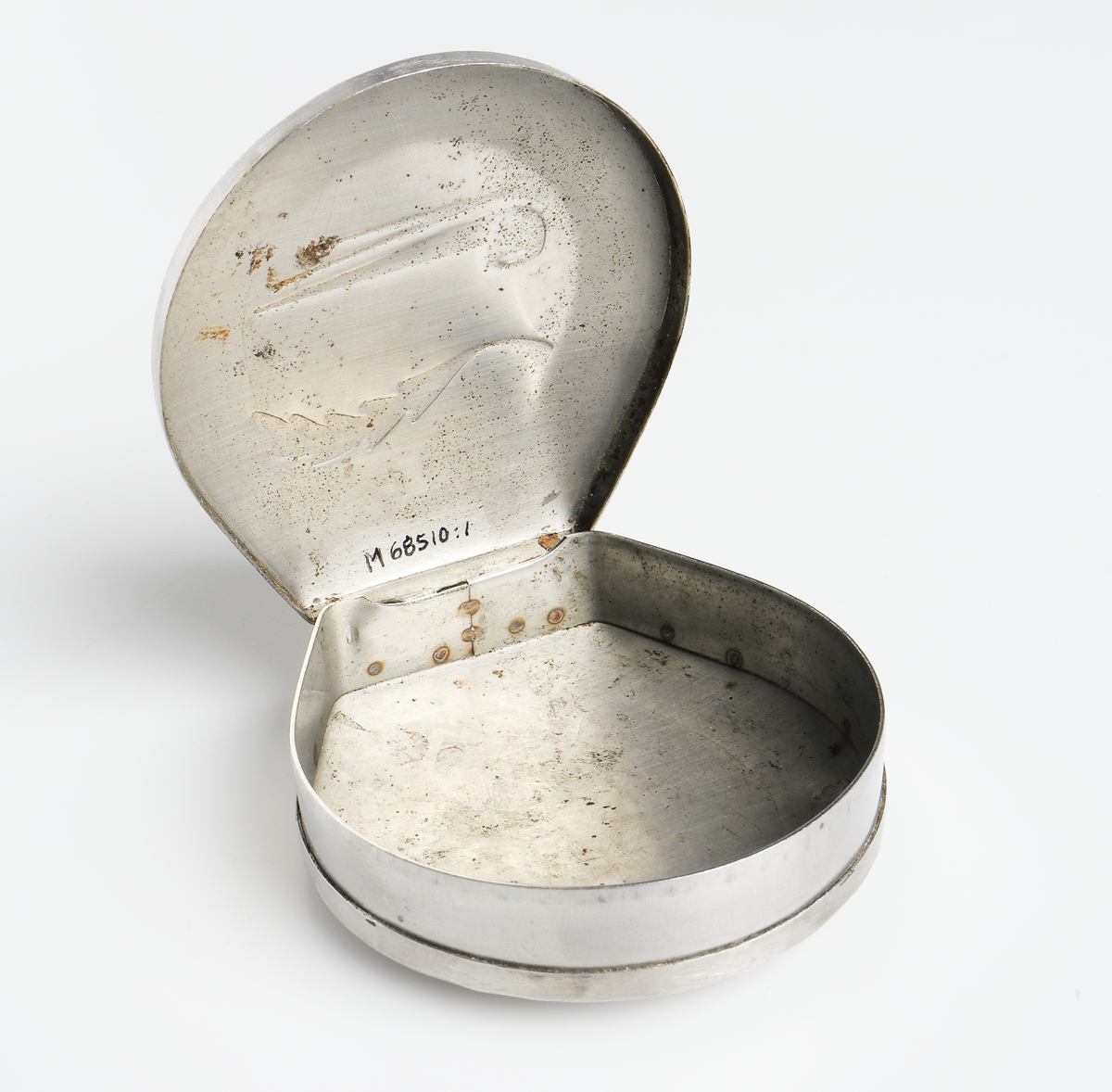 Dosa i metall. Lock med gångjärn. På locket ett pressat motiv föreställande en pipa och ett tobaksblad.