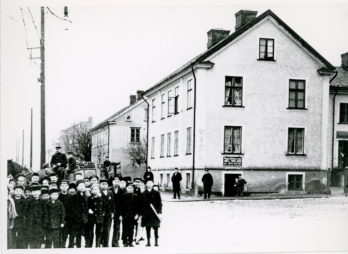 Hörnet Nygatan/Bäckgatan, ca 1910.
En bryggarkärra rundar just hörnet vid "Magnus Johanssons Mjölk, Smör, Bröd och Ostaffär, där en poliskonstapel har stannat till. En skock pojkar är mycket intresserade av fotografen.