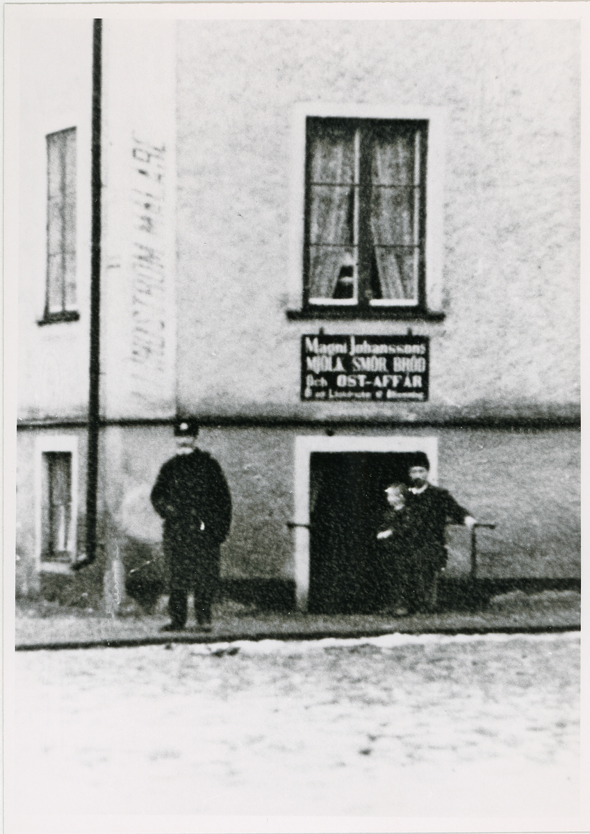 Hörnet Nygatan/Bäckgatan, ca 1910.
En bryggarkärra rundar just hörnet vid "Magnus Johanssons Mjölk, Smör, Bröd och Ostaffär, där en poliskonstapel har stannat till. En skock pojkar är mycket intresserade av fotografen.