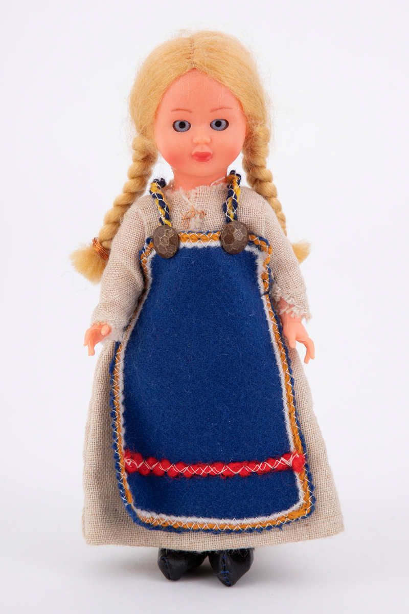 En sovedukke med drakt som etterligner en drakt fra skuespillet Spelet om Heilag Olav, også kalt Stiklestadspelet. Dukken er lagd av celluloid og har lange lyse fletter, lang beige kjole og blått forkle.