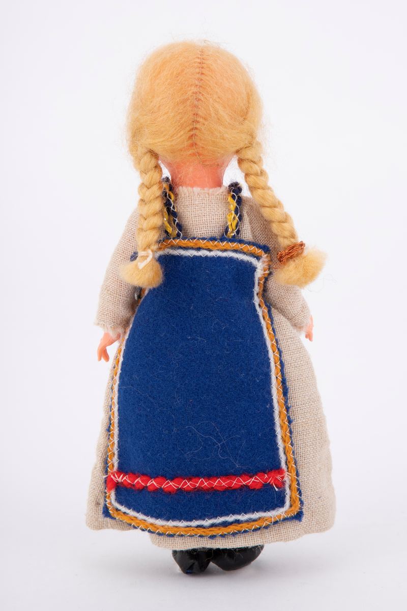 En sovedukke med drakt som etterligner en drakt fra skuespillet Spelet om Heilag Olav, også kalt Stiklestadspelet. Dukken er lagd av celluloid og har lange lyse fletter, lang beige kjole og blått forkle.
