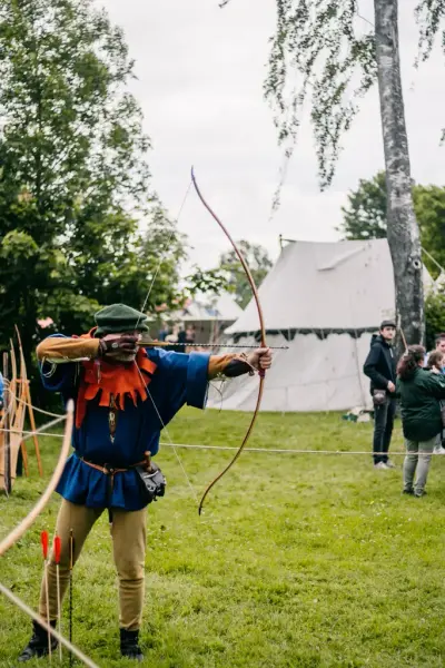Bueskytter i drakt fra 1400-tallet. Blå jakke, rød hette og beige hoser