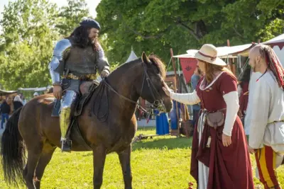 Ridder i platerustning til hest. Dame i rød kjole klapper hesten