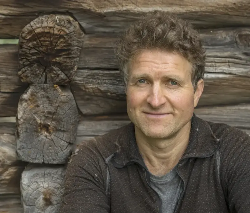 Portrett av en mann foran en tømmervegg