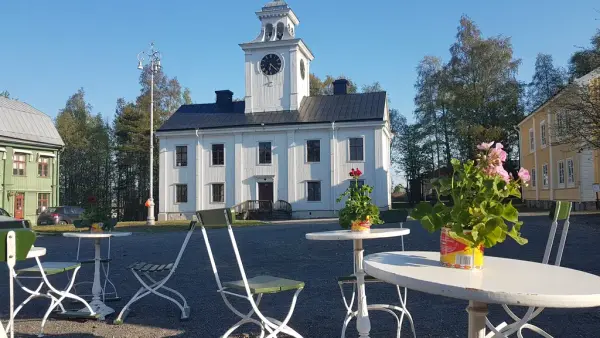 Kaféstolar och bord med blommor i förgrunden och rådhuset samt två andra byggnader i bakgrunden.