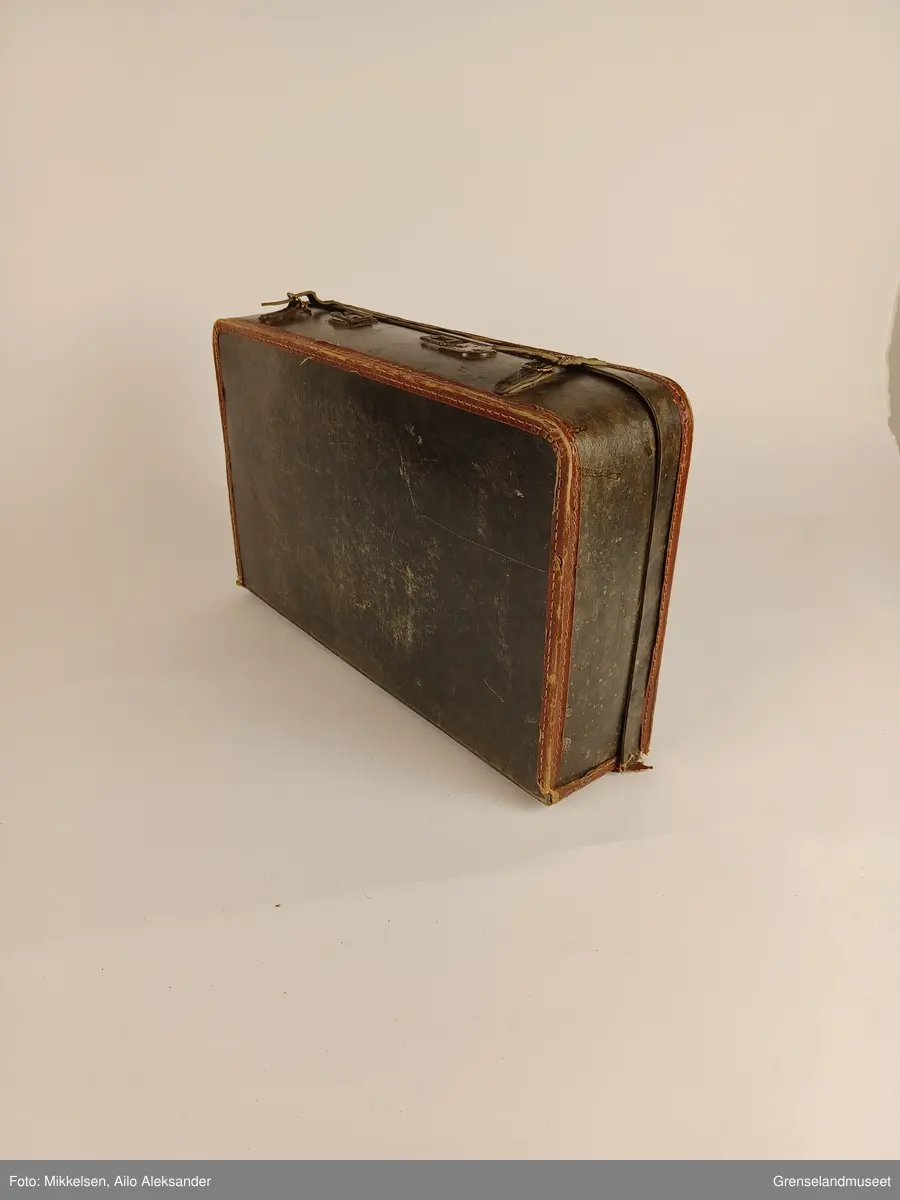 Gjenstanden er en reisekoffert i lær med påsydd lærreimer med beltehanker til å lukke og åpne kofferten med. Bolter og spiker som er med på holde den sammen er nå rustent. Lærhandtaket som kofferten engang hadde var ikke tilstede da gjenstanden ble mottatt av museet. Koffertens ytterside av lær er full av riper, flekker og rifter noe som viser at den har vært mye brukt opp igjennom årene. Læret på ytter- og innsiden er tørt og viser ingen tegn til vedvarende mugg eller fukt skade. 

Koffertens innside har rifter og bruksmerker. Læret som er festet til koffertens innside bunn, vegger og lokk har begynt å løsne i kantene. Sømmene som holder kofferten er frynsete på noen steder, men holder fremdeles kofferten sammen i solid tilstand. Ingenting ser ut til å mangle eller være betydelig skadet bortsatt fra manglende bærereim av lær. 