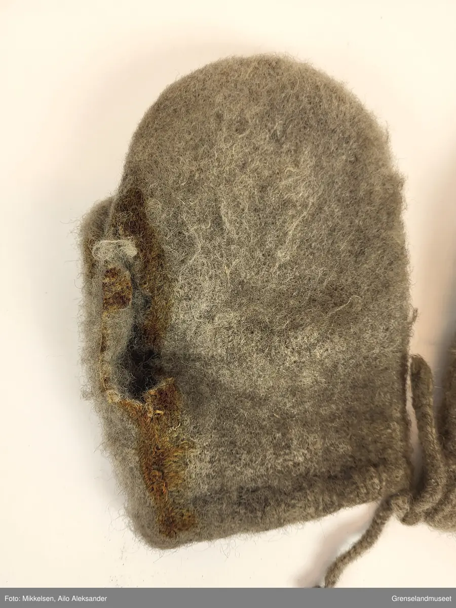 De to gjenstandene er et par grå ullvotter. Ullvottenes tilstand er ikke i god ettersom at den har flere svertede flekker og flere hull. Spesielt for votten tilhørende venstre hånd er det en stor rift fra der pekefinger ville ligge og inn over tommelen. De to vottene er festet sammen med snorer som er strikket inn i ermene.   