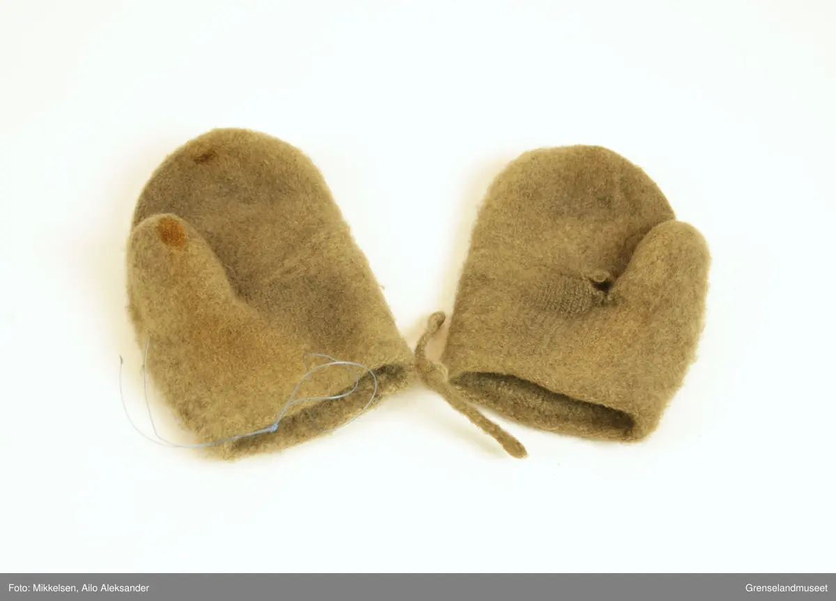 De to gjenstandene er et par grå ullvotter. Ullvottenes tilstand er ikke i god ettersom at den har flere svertede flekker og flere hull. Spesielt for votten tilhørende venstre hånd er det en stor rift fra der pekefinger ville ligge og inn over tommelen. De to vottene er festet sammen med snorer som er strikket inn i ermene.   