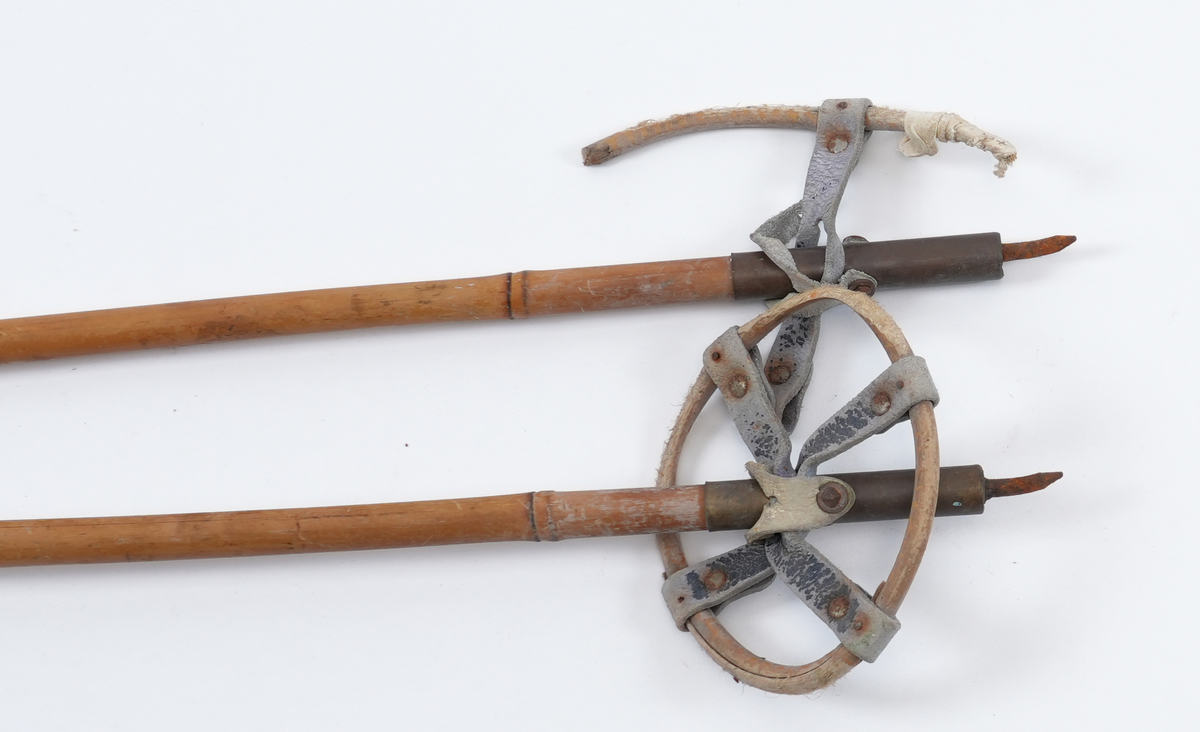 Bambusstavar med skinnreimer som handtak. Skinnreimene er kvite og festa til bambusstavane med ei nagle. På bambusstavane er det spor etter klistermerker med ukjend motiv, men med påskrift "Standard" og "Made in Norway". Trinser av bambus og lær. 