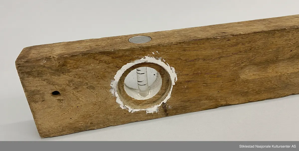 Fabrikkprodusert vater i løvtre, glass og blikk. På ene siden av vater er glass til vertikal libelle borte, glass finnes på andre siden - reparert med sparkelmasse? Signartur/logo innstanset på blikkplate over horisontal libelle. Opphengshull i ene enden.