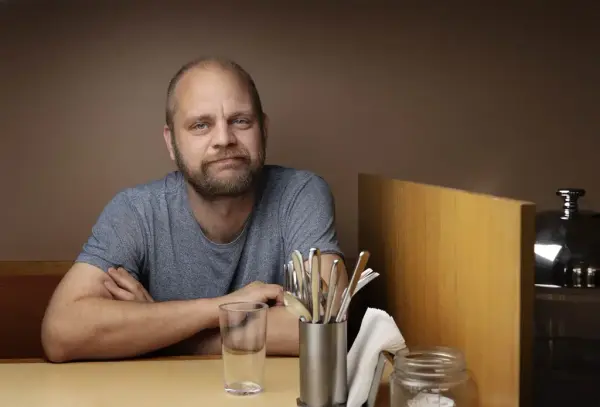 Mimir Kristjansson i grå t-skjorte sitjande ved eit kafebord