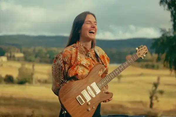Symre Taugbøl Bang med gitar, og eit naturlandskap i bakgrunnen