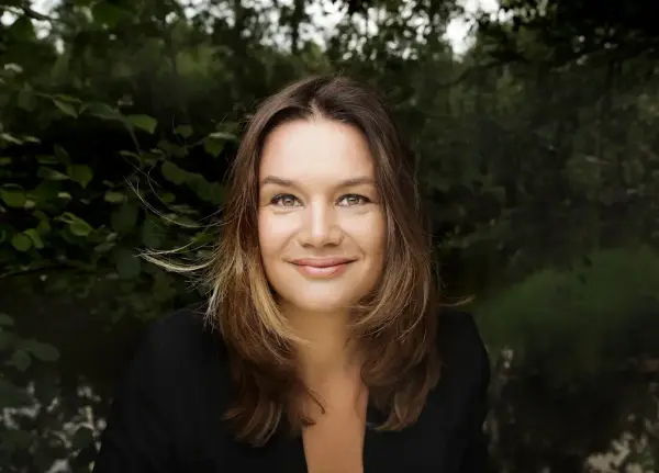 Portrettfoto av Ruth Lillegraven med svart jakke framom nokre grøne lauvtre