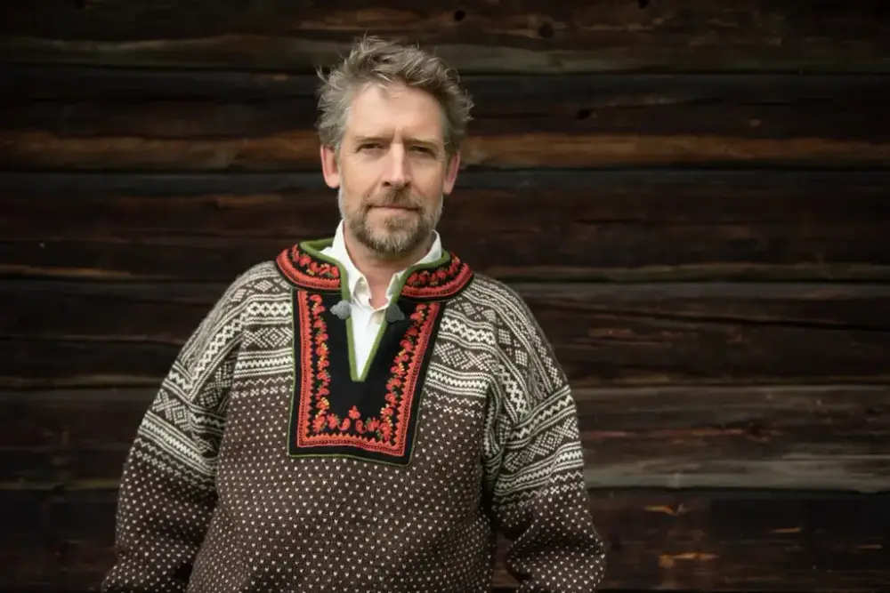 Åsmund Nordstoga med lusekofte framom eit tømmerhus