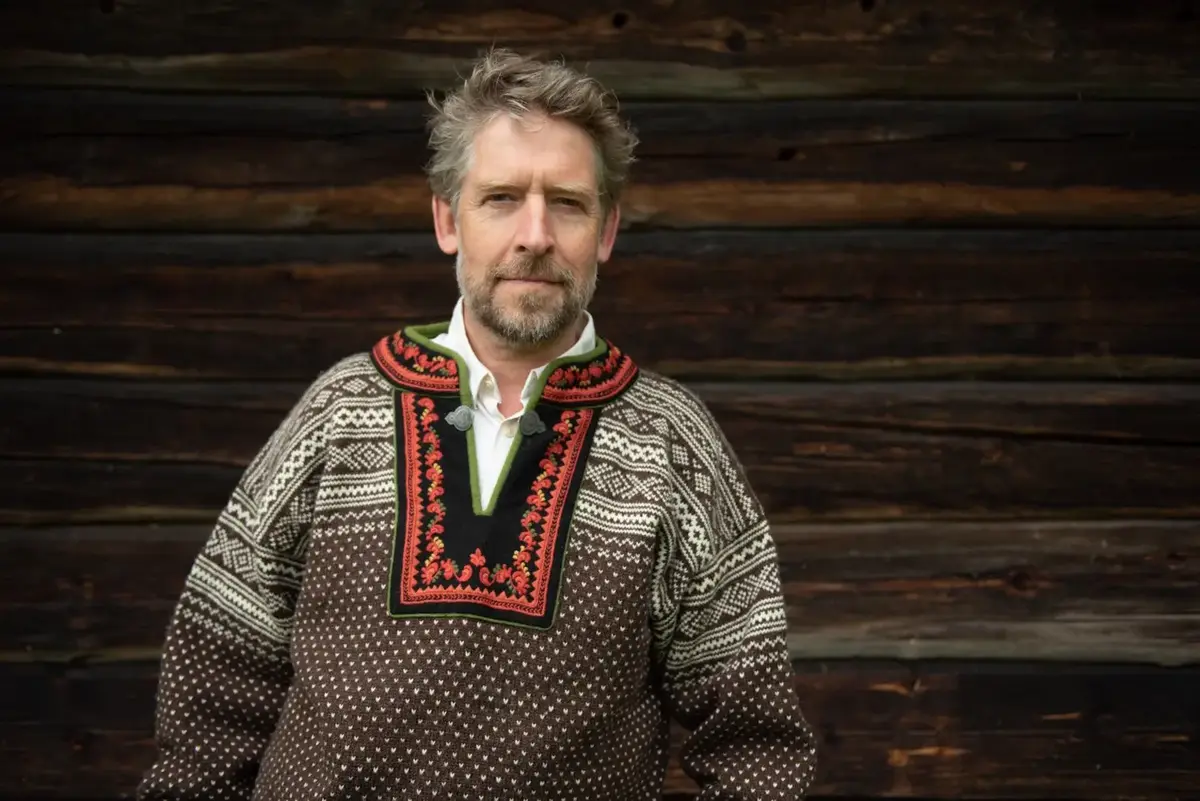 Åsmund Nordstoga med lusekofte framom eit tømmerhus