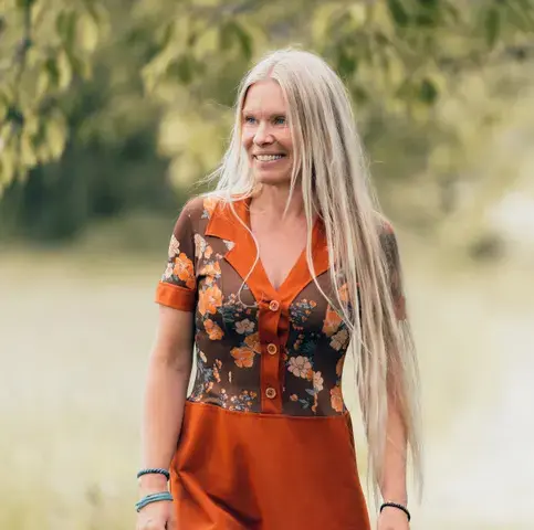 Anne Gravir Klykken i blomstrete kjole med tre og eng i bakgrunnen