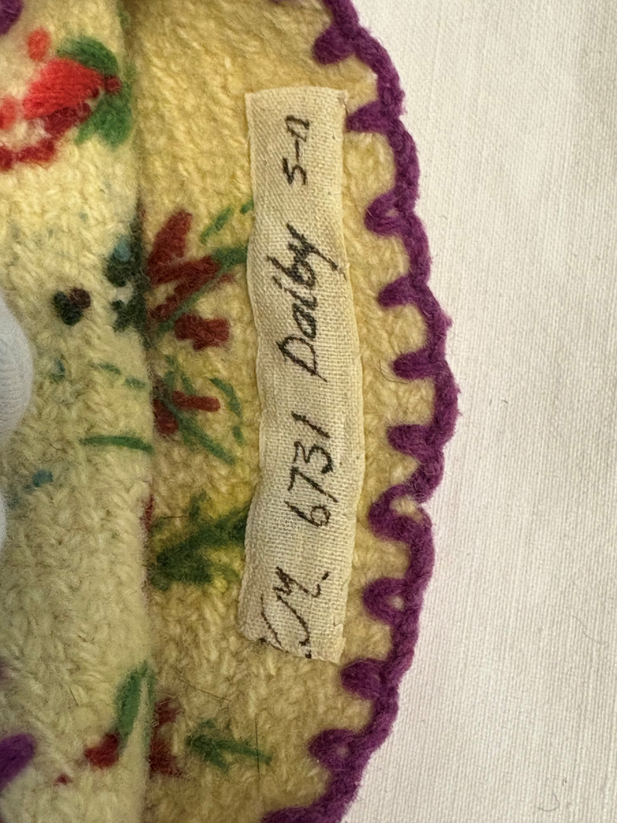 Vit nålbunden vante med broderi i blomstermotiv. Lång mudd med dekorationer runt om. Även dekorationer på tummarna. Högervante.