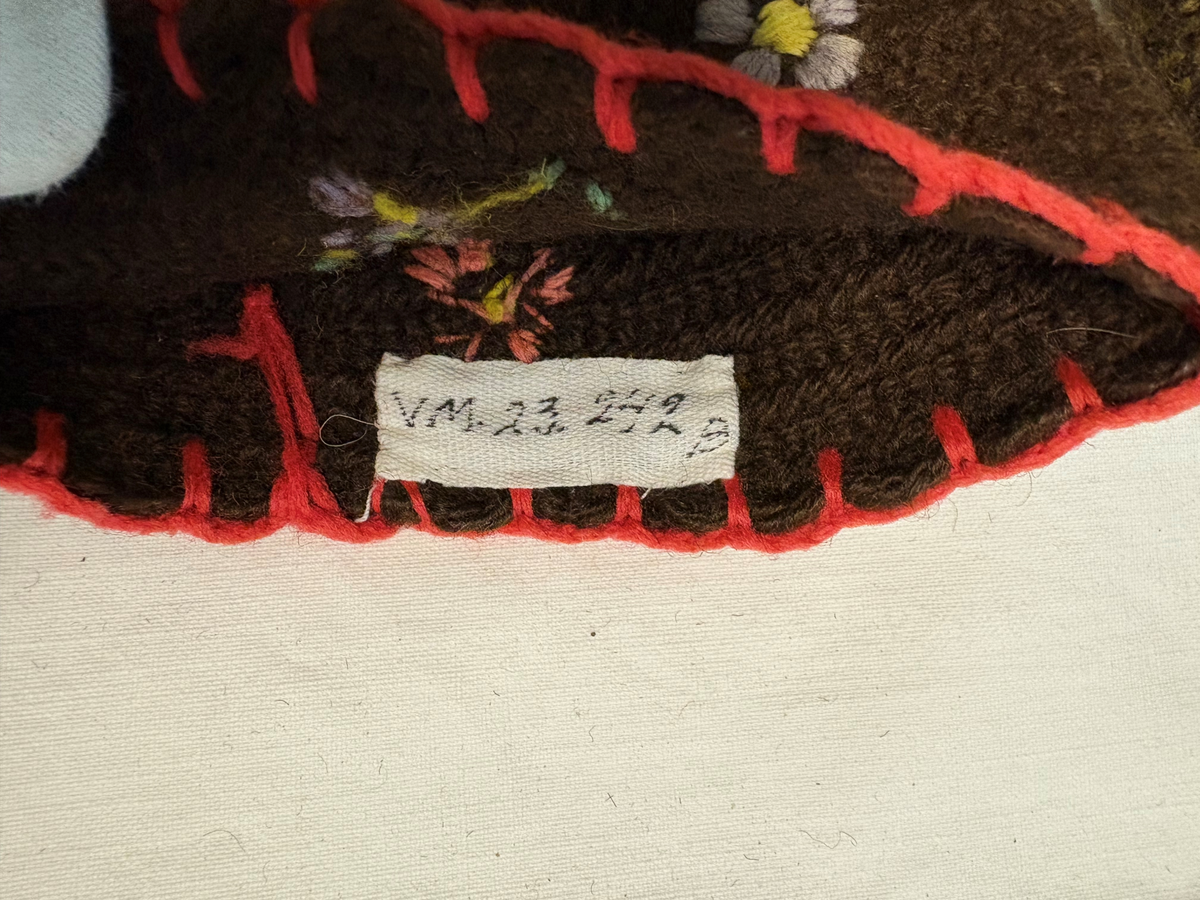 Tumvantar av brunt yllegarn. Broderi i rött, grönt, blått, rosa, gult och lila.