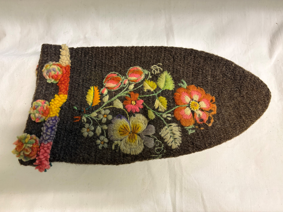 Brudgumsvantar, bruna. Broderade med yllegarn i färgerna lila, gult, grönt, vitt och blått i schattersöm och stjälksöm. Nedvikt kant.