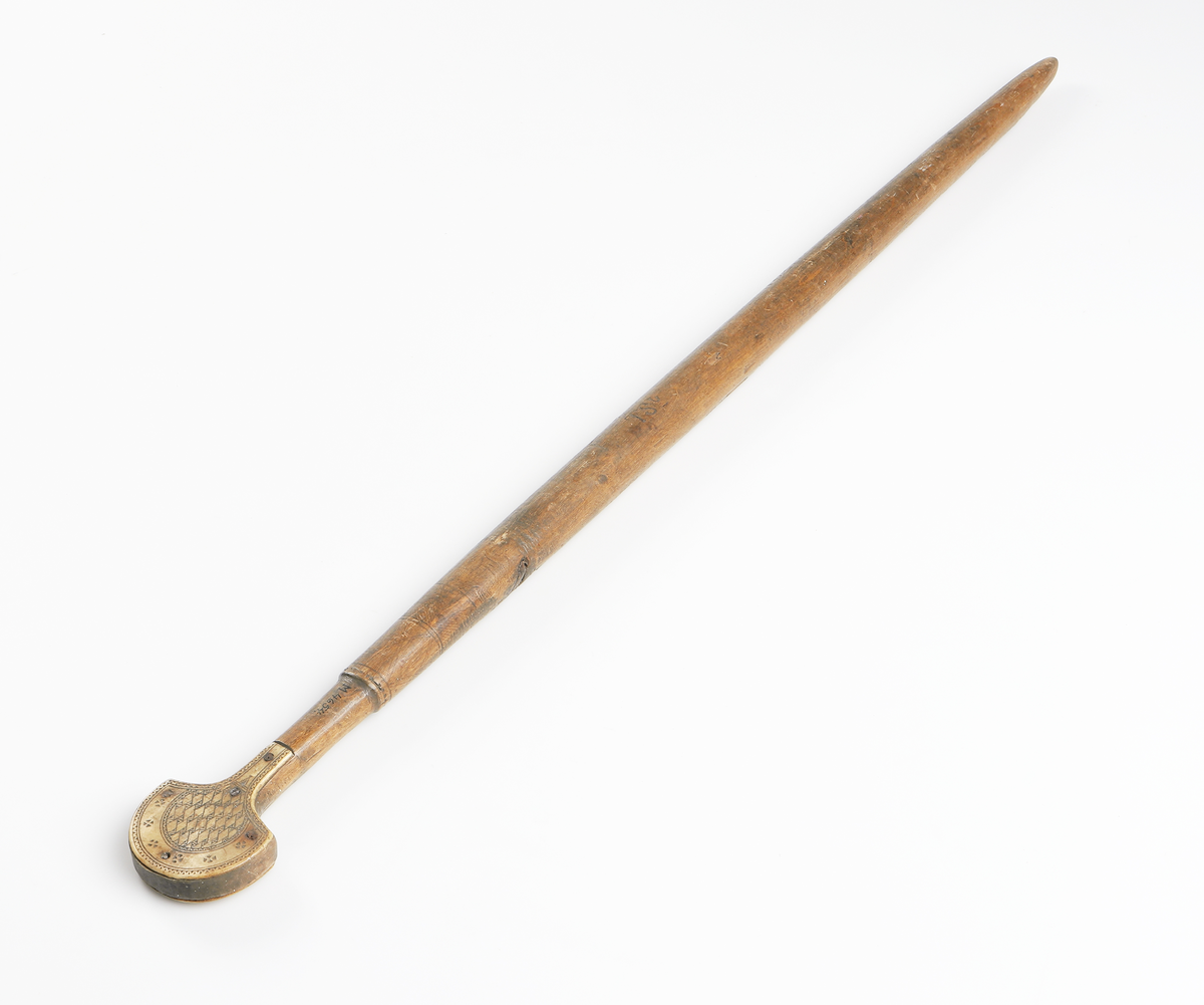 Käpp av trä med benförsedd knopp. Benstyckerna, ett på vardera sidan, är dekorerade med geometriska figurer, fastsatta med fem spikar. Inuti käppen har man lagt i stenar eller liknande så att den skramlar när man rör den. Från Gällivare.