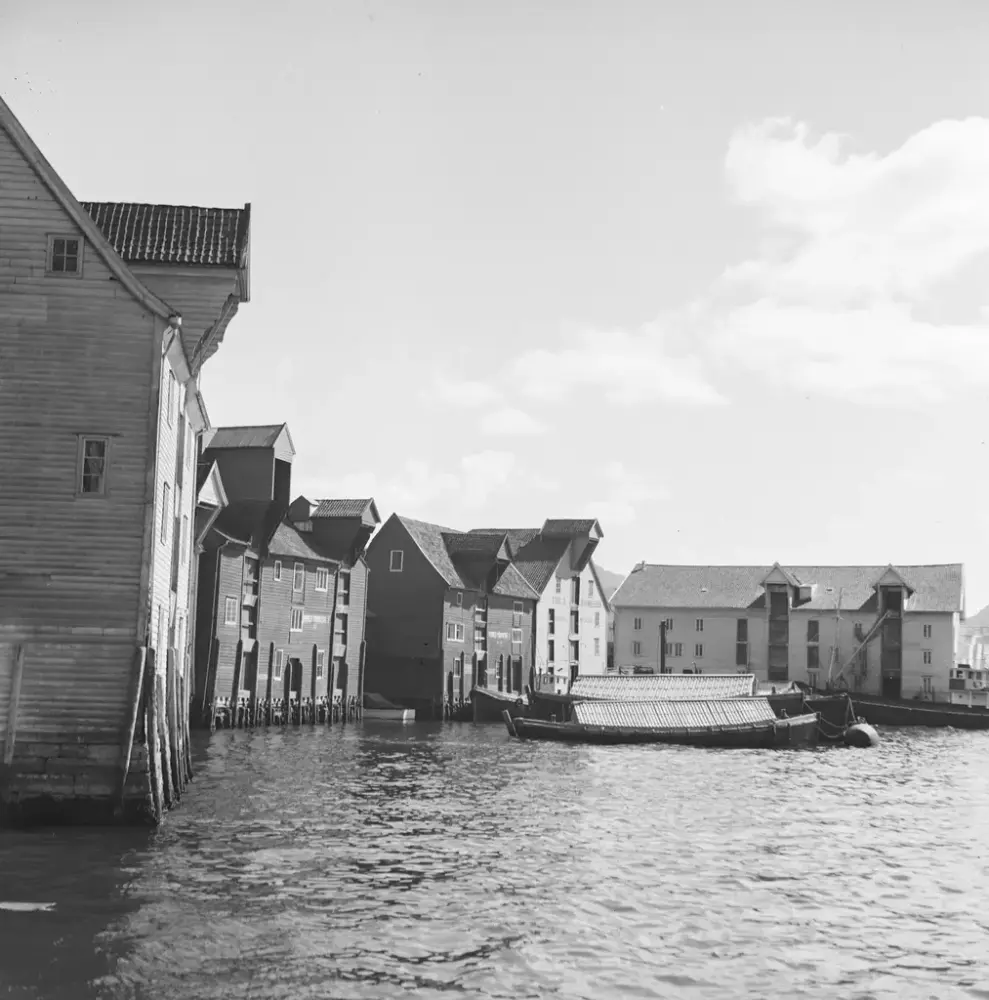 Foto viser flere sjøboder med sjø foran og et par jekter