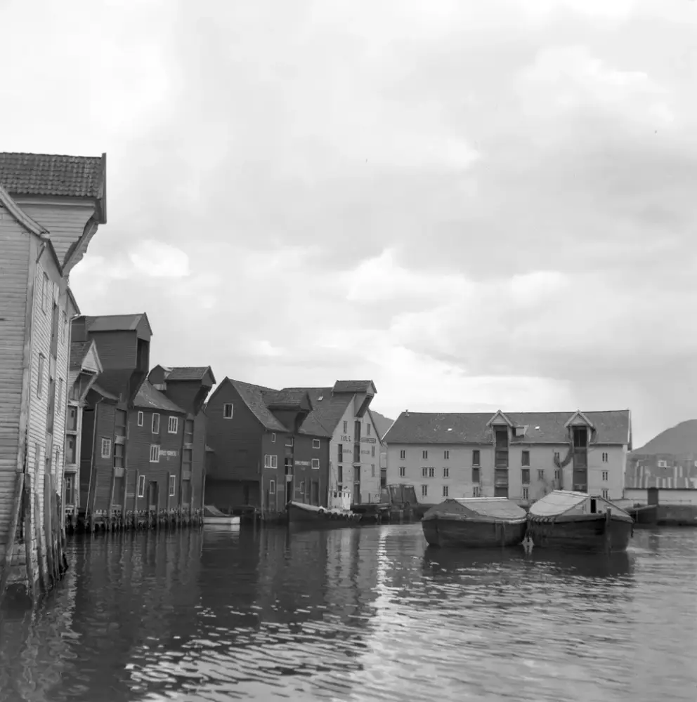 Sort hvitt bilde viser sjøboder med to jakter foran