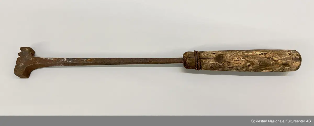 Svijern med dreid treskaft. Ved tangen er skaftet forsterket med to runder ståltråd. Toppen av skaftet har innskåret en linje (rundt skaftet). Initialer svijern: NOØ
