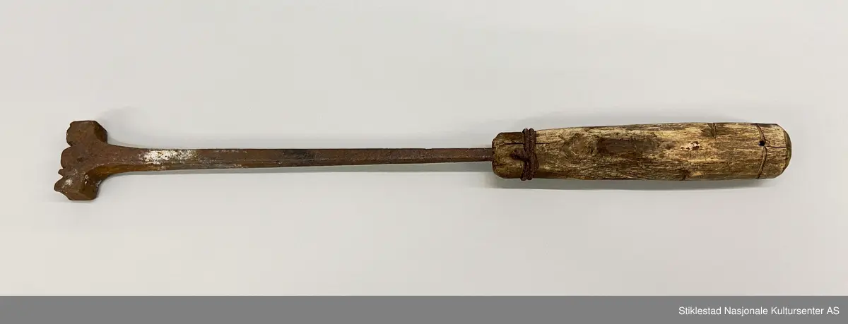Svijern med dreid treskaft. Ved tangen er skaftet forsterket med to runder ståltråd. Toppen av skaftet har innskåret en linje (rundt skaftet). Initialer svijern: NOØ