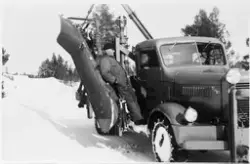 En mann står på stigtrinnet til en parkert brøytebil