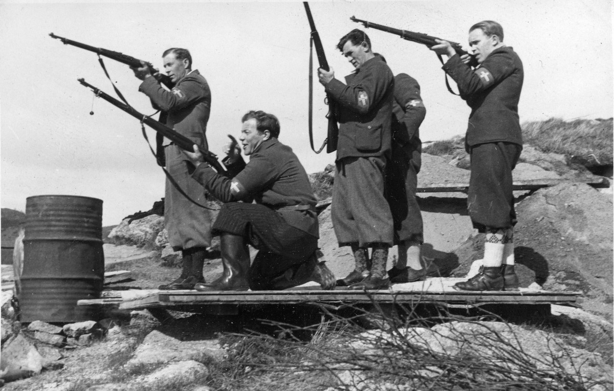 Menn med milorgs armbind fotografert mens de trener med gevær.