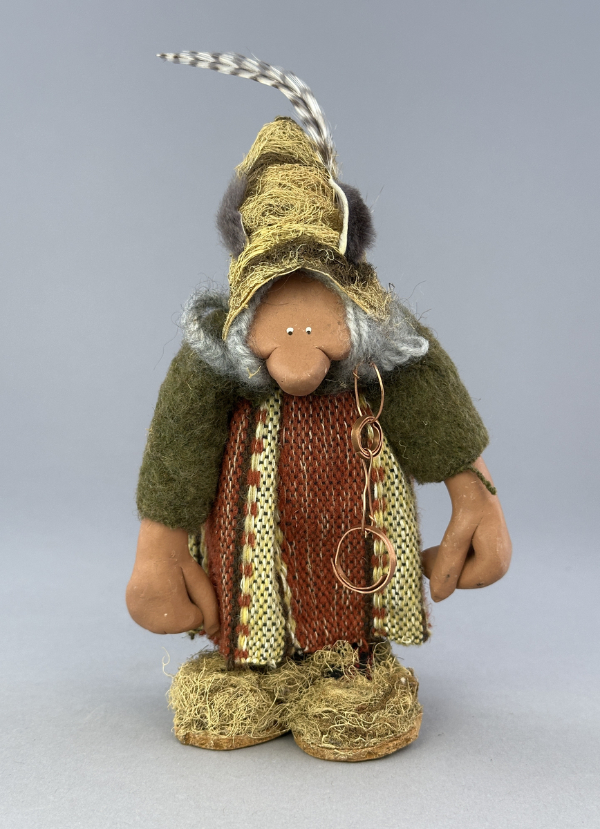Krokig trollgumma med stora fötter och händer.  Är klädd i randig vävd kjol och grön jacka. Har lavbeklädd mössa med fjäder, lavbeklädda skor samt örhänge av koppar.

