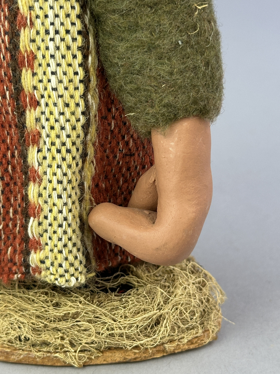 Krokig trollgumma med stora fötter och händer.  Är klädd i randig vävd kjol och grön jacka. Har lavbeklädd mössa med fjäder, lavbeklädda skor samt örhänge av koppar.

